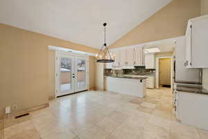 Dining area with french doors, kitchen peninsula, hanging light fixtures, tasteful backsplash, and white cabinetry