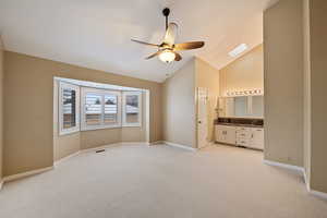 Owner's bedroom with vaulted ceiling with skylight, ceiling fan, light carpet, and connected bathroom