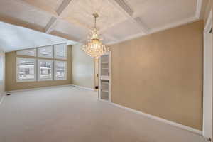 Carpeted dining/living room featuring crown molding, beamed ceiling, coffered ceiling, and a notable chandelier