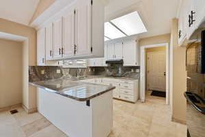 Kitchen with decorative backsplash, dark stone countertops, white cabinetry, and kitchen peninsula