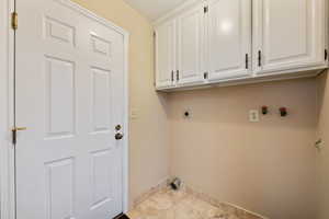 Mud room/laundry room featuring hookup for an electric dryer, a textured ceiling, cabinets, and light tile patterned flooring