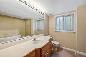 Bathroom with vanity, a jetted bathtub, toilet, and a textured ceiling