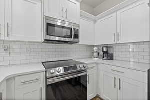 Kitchen featuring decorative backsplash, white cabinetry, and appliances with stainless steel finishes