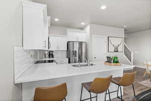 Kitchen featuring white cabinets, sink, stainless steel fridge with ice dispenser, kitchen peninsula, and a breakfast bar area