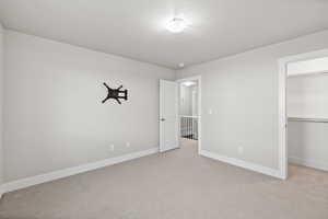 Unfurnished bedroom featuring light colored carpet, a walk in closet, and a closet