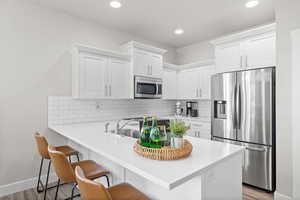 Kitchen with kitchen peninsula, light wood-type flooring, a breakfast bar, stainless steel appliances, and white cabinets