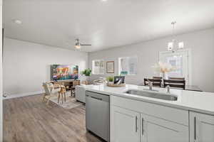 Kitchen with dishwasher, sink, pendant lighting, white cabinets, and ceiling fan with notable chandelier