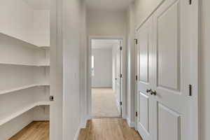 Hall with storage/pantry closet and linen closet with light wood-type flooring