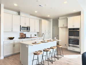 Kitchen featuring stainless steel appliances, an island with sink, a kitchen bar, and white cabinetry