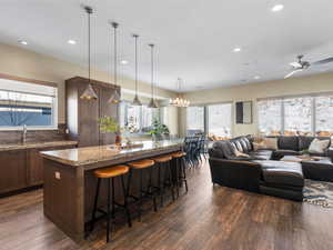 Kitchen with sink, light stone counters, decorative light fixtures, a breakfast bar, and ceiling fan with notable chandelier