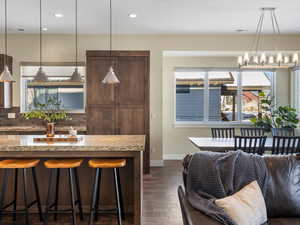 Kitchen with light stone countertops, dark wood-type flooring, pendant lighting, a breakfast bar area, and decorative backsplash