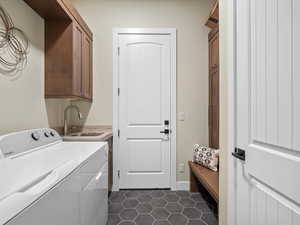 Washroom with cabinets, dark tile patterned floors, washer and dryer, and sink