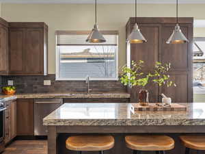 Kitchen with dishwasher, dark wood-type flooring, sink, tasteful backsplash, and a kitchen bar