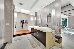 Bathroom featuring a skylight, vanity, concrete floors, and tile walls