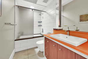 Full bathroom with tile patterned floors, vanity, toilet, and enclosed tub / shower combo