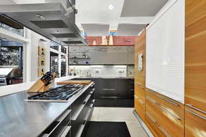 Kitchen featuring gray cabinetry, backsplash, stainless steel gas stovetop, island range hood, and light tile patterned flooring