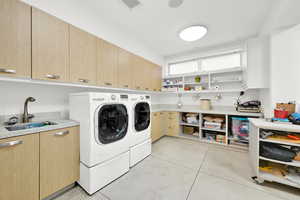 Washroom with cabinets, light tile patterned floors, washing machine and dryer, and sink