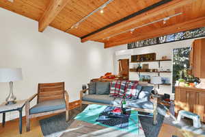 Living room with beam ceiling, rail lighting, wood ceiling, and a wall mounted air conditioner