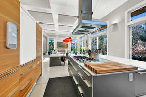 Kitchen with island exhaust hood, wooden walls, light tile patterned floors, a center island, and stainless steel gas stovetop