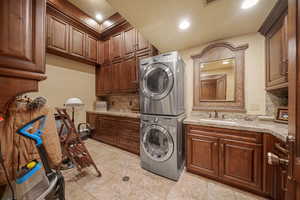 Laundry area with sink, cabinets, and stacked washer and clothes dryer