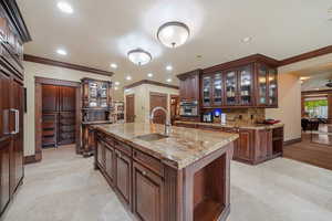 Kitchen with dark brown cabinetry, sink, oven, a kitchen island with sink, and ornamental molding