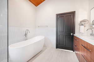 Bathroom featuring a bathtub, vanity, lofted ceiling, tile patterned flooring, and tile walls