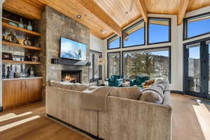 Living room featuring light wood-type flooring, beam ceiling, a stone fireplace, wood ceiling, and high vaulted ceiling