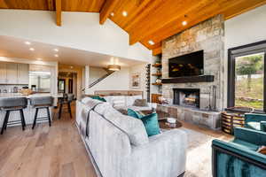 Living room with high vaulted ceiling, light hardwood / wood-style flooring, beamed ceiling, wooden ceiling, and a fireplace