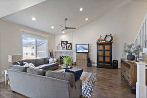 Living room with a fireplace, ceiling fan, dark wood-type flooring, and vaulted ceiling