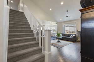 Stairway with high vaulted ceiling, wood-type flooring, and ceiling fan with notable chandelier