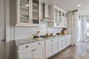 Kitchen featuring stainless steel gas stovetop, wall chimney exhaust hood, white cabinets, and light stone countertops