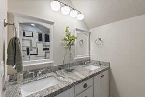 Bathroom with a textured ceiling, vanity, and vaulted ceiling