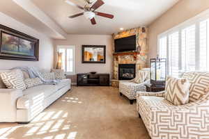 Carpeted living room featuring a stone fireplace, ceiling fan, and plenty of natural light