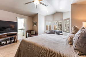 Carpeted bedroom featuring ceiling fan, lofted ceiling, and ensuite bath