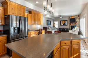 Kitchen featuring ceiling fan, a kitchen island, a stone fireplace, and stainless steel fridge with ice dispenser