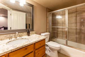 Full bathroom featuring vanity, bath / shower combo with glass door, a textured ceiling, and toilet