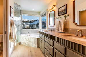 Bathroom featuring hardwood / wood-style floors, a relaxing tiled tub, toilet, and vanity