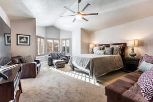 Carpeted bedroom featuring ceiling fan, a textured ceiling, and vaulted ceiling