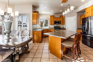 Kitchen with appliances with stainless steel finishes, decorative light fixtures, a kitchen island, and light tile patterned flooring