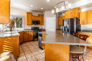 Kitchen featuring a kitchen bar, appliances with stainless steel finishes, decorative light fixtures, a center island, and light tile patterned flooring