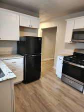 Kitchen with a textured ceiling, light stone counters, white cabinetry, and stainless steel appliances