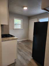 Kitchen featuring light stone countertops, light hardwood / wood-style flooring, black appliances, and a textured ceiling