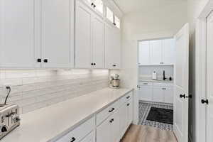 Kitchen featuring decorative backsplash, white cabinetry, light hardwood / wood-style flooring, and sink