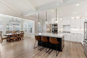 Kitchen with beam ceiling, pendant lighting, a center island with sink, white cabinets, and stainless steel microwave