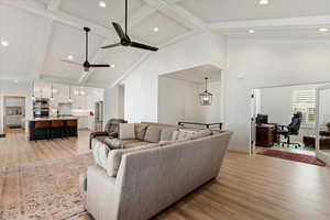 Living room featuring beam ceiling, ceiling fan with notable chandelier, light hardwood / wood-style floors, and high vaulted ceiling