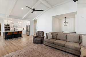 Living room with high vaulted ceiling, ceiling fan with notable chandelier, sink, light hardwood / wood-style flooring, and beam ceiling