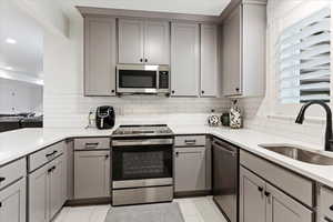 Kitchen featuring gray cabinetry, a wealth of natural light, sink, light tile patterned floors, and appliances with stainless steel finishes