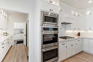 Kitchen featuring custom range hood, stainless steel appliances, white cabinetry, and light hardwood / wood-style flooring