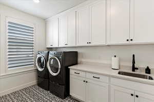 Laundry room with washing machine and dryer, sink, light tile patterned floors, and cabinets