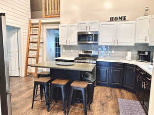 Kitchen with hardwood / wood-style floors, a center island, stove, white cabinetry, and a breakfast bar area